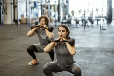 fit man and woman doing a squat with double kettlebells