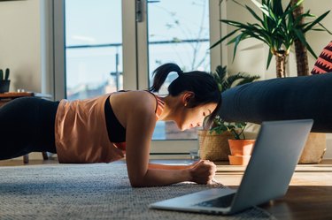 Young woman doing plank exercise in font of laptop at home