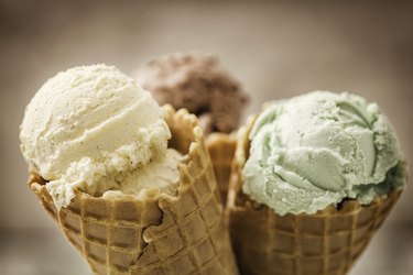 a close up photo of Vanilla, Chocolate and Pistachio Ice Cream, a food that can cause stomach pain, in waffle cones with a brown background