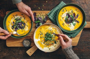 Hands holding bowls of Instant Pot Creamy Roasted Pumpkin Soup