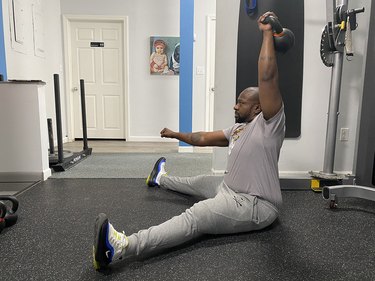 Man doing a seated overhead press with a kettlebell during an arm workout
