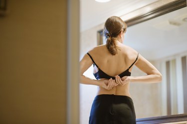back view of a person fastening their bra in front of the mirror