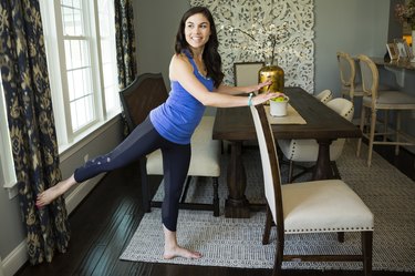 Woman doing a barre workout with a chair in her dining room