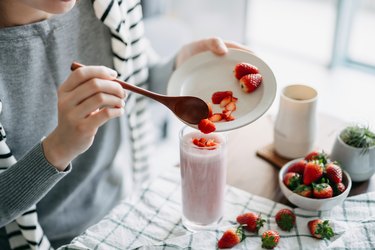 Close up of young woman making fresh and healthy strawberry smoothie for breakfast