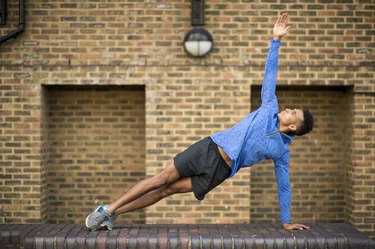 Man doing a side plank in front of brick wall, Wapping, London, UK