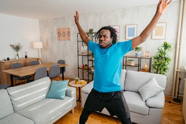 Person wearing blue T-shirt and black shorts doing jumping jacks in living room as part of a morning workout for weight loss