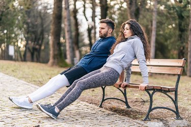 Couple doing triceps dips on a park bench