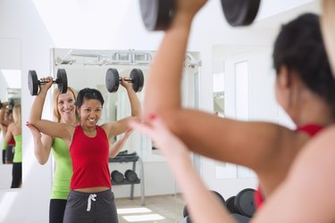 a woman having a hard time with an overhead press exercise, working with a female trainer