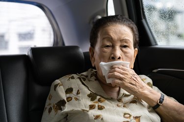 Older adult sitting in the backseat of a car and holding a napkin over their mouth because they have excessive saliva