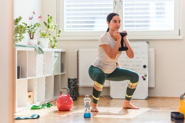 young asian woman doing a sumo squat with a dumbbell as part of an inner thigh workout in her home gym
