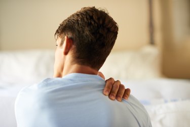 back view of a person with short brown hair holding their shoulder because they have shoulder pain from sleeping