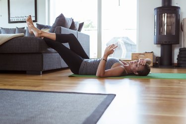 Tired woman using mobile phone while lying on exercise mat in living room