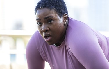 Person in a larger body wearing a purple long-sleeve shirt with short hair and earrings sweating during a workout