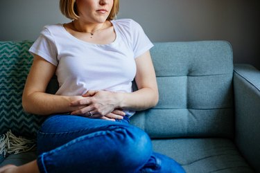 woman sitting on the couch and holding her stomach in pain from tenesmus