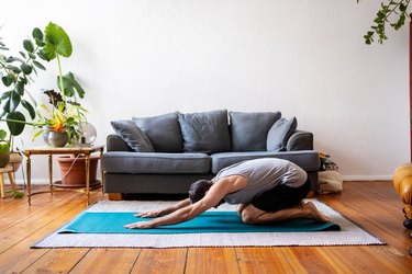 man doing child's pose on a blue yoga mat in living room