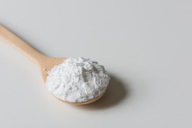 Close-up of raw cornstarch in wooden spoon on a cream tabletop