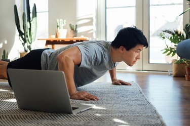Cropped shot of young man doing push-up in front of laptop at home