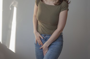 a person wearing a green t-shirt and jeans with their hands over their crotch area because they have an itchy pubic area