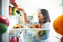 Woman picks out a handful of fruits and veggies from the fridge